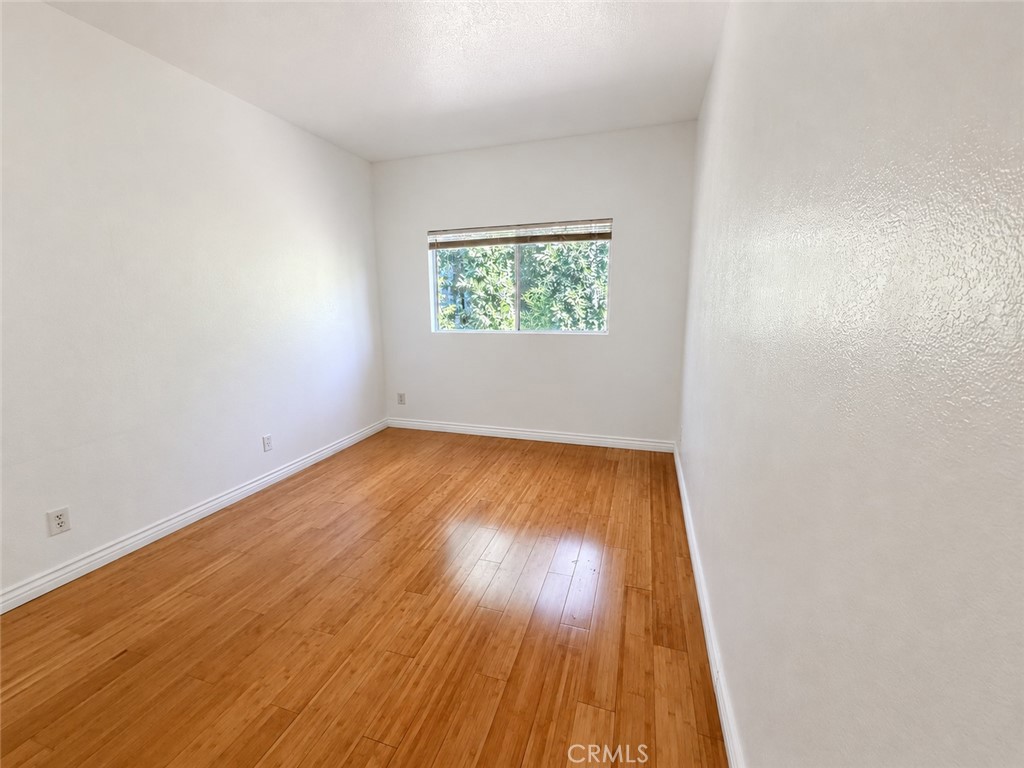 Vacant bedroom with warm hardwood floors and a window overlooking leafy greenery.