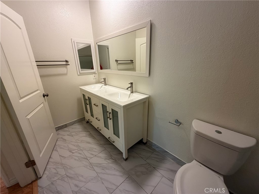 Bathroom with a double-sink vanity, large mirror, and marble-look tile floor.