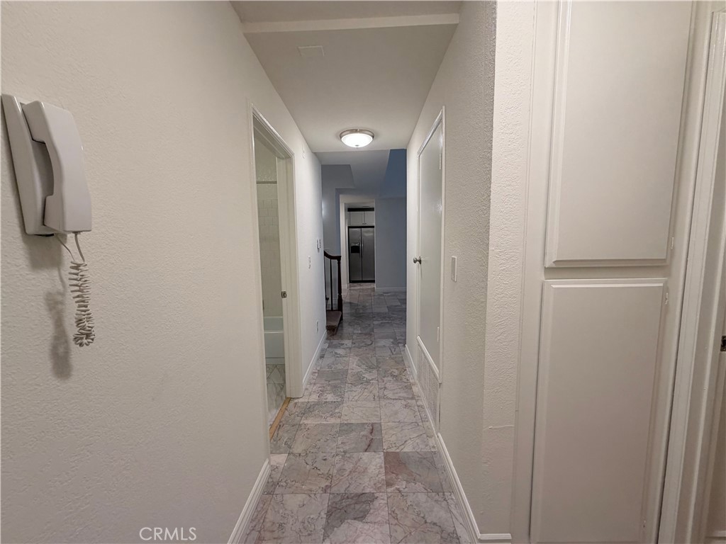 Apartment hallway with marble-pattern tile flooring, a wall intercom, and a stainless-steel refrigerator at the far end.