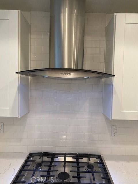 Kitchen with a stainless steel range hood over a gas cooktop and white subway tile backsplash.