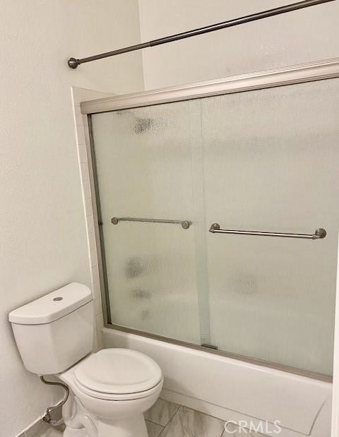Bathroom with a toilet beside a bathtub enclosed by frosted sliding glass doors.