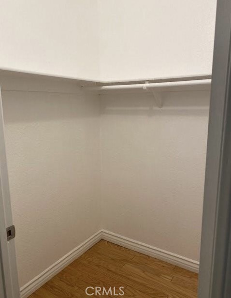 Empty walk-in closet with a white shelf and hanging rod above wood flooring.