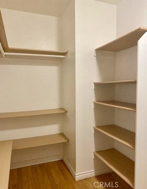 Walk-in closet with built-in shelving and wood flooring.
