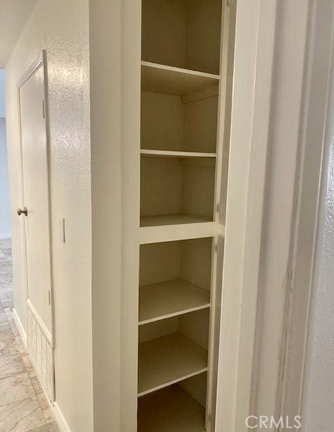 Empty built-in hallway closet with multiple open shelves beside a white door.