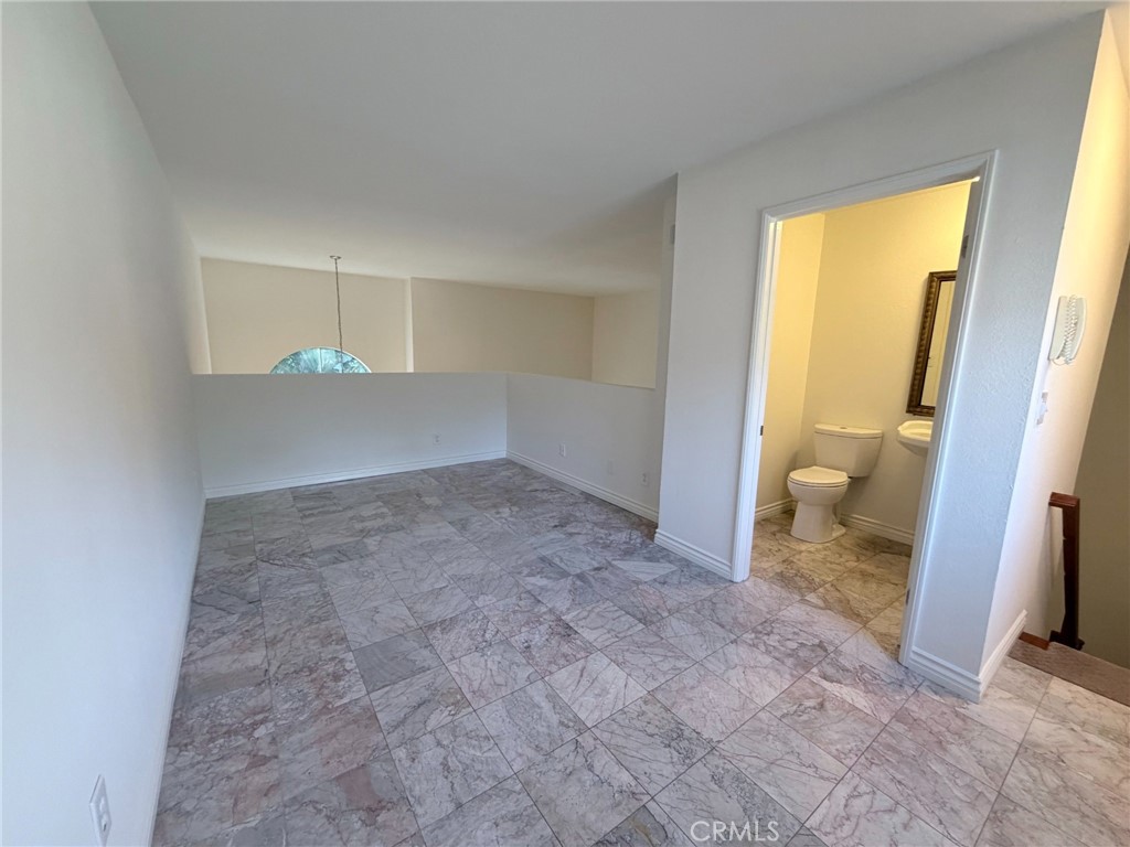 Empty tiled room with a half-height partition, open bathroom doorway, and stairs.