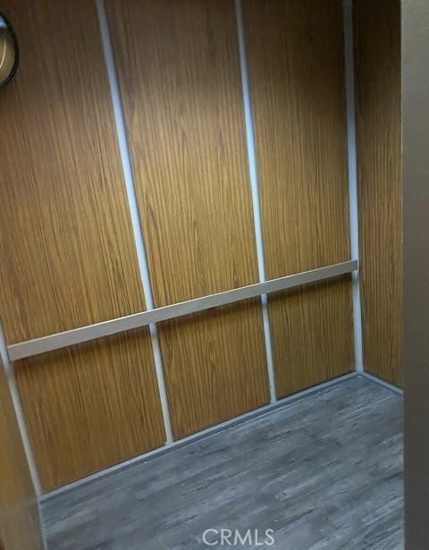 Small elevator with wood-paneled walls, a metal handrail, and gray plank flooring.