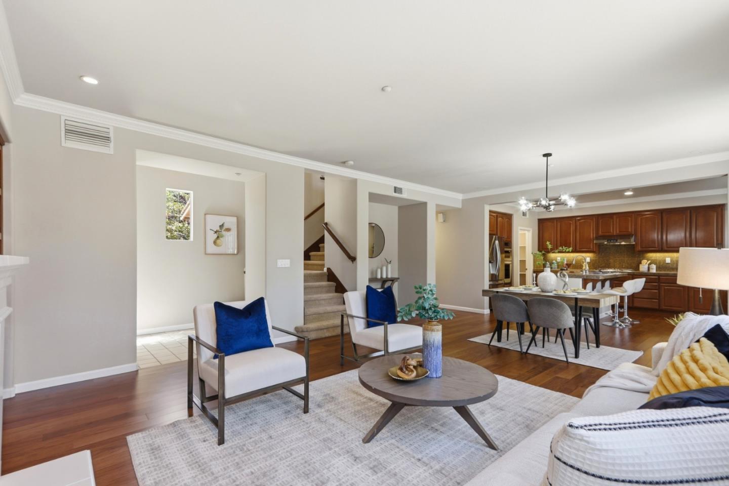 Open-plan living room and kitchen with hardwood floors, blue accent pillows, and dark wood cabinets.