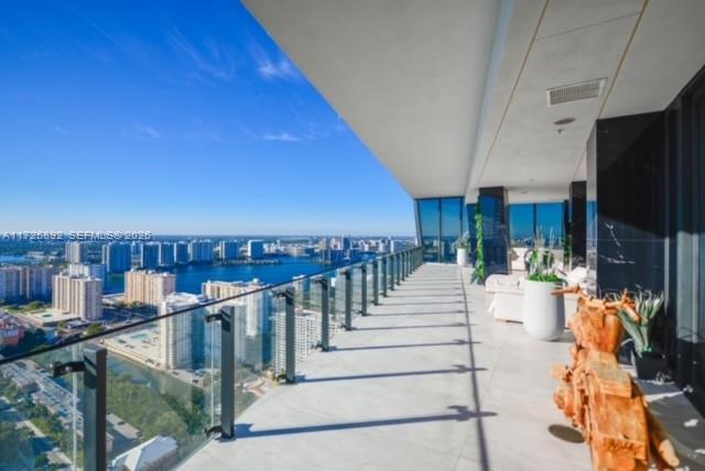 High-rise balcony with glass railing, patio seating, and expansive ocean and city views.