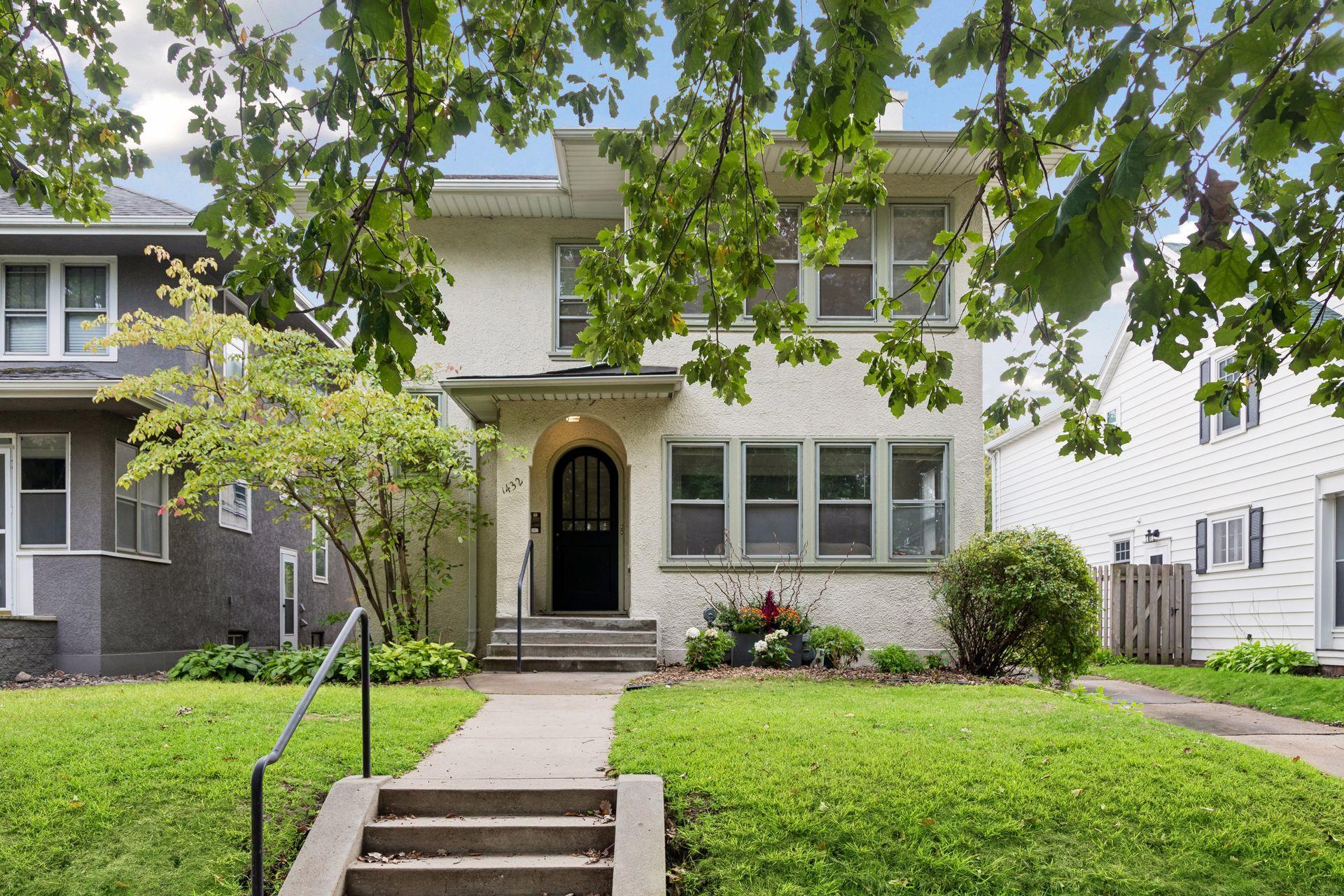 Two-story stucco home with an arched black entry, front steps, and leafy trees.