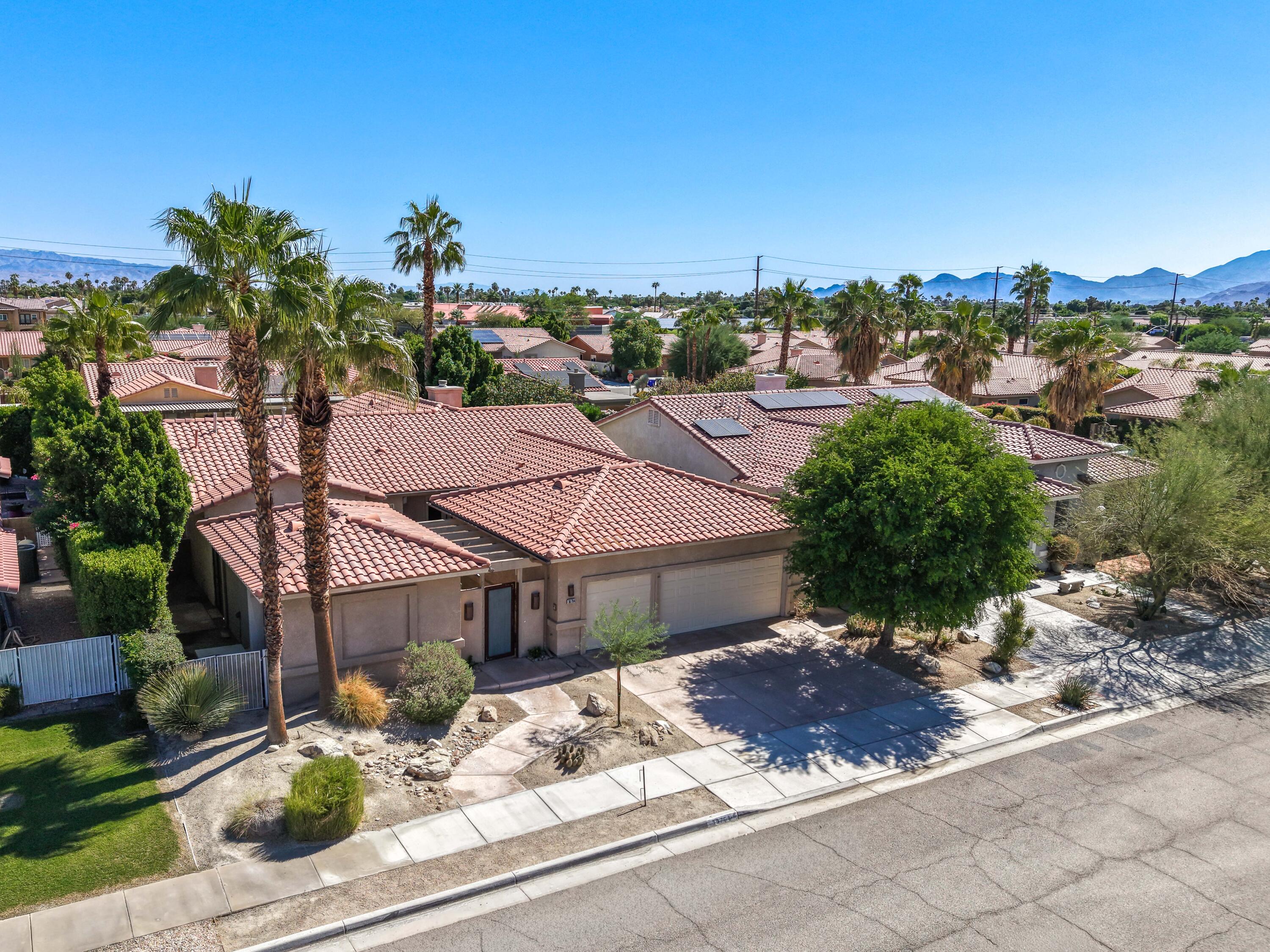 Aerial view of a tile-roof home and palm-lined neighborhood with mountains beyond.