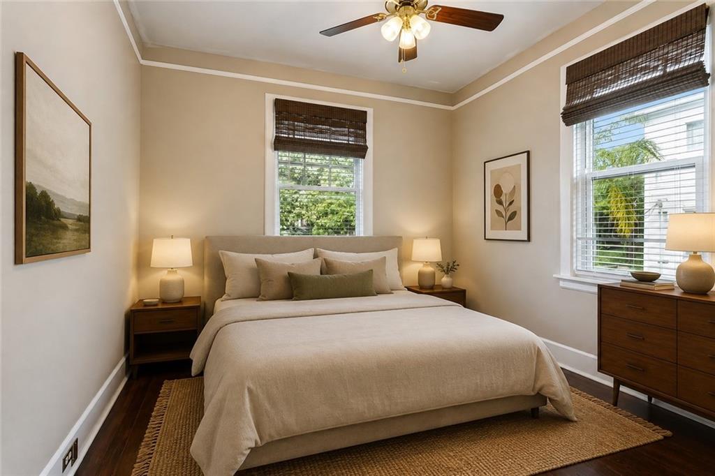Staged bedroom with a neutral bed, dark wood nightstands, and windows with woven shades.