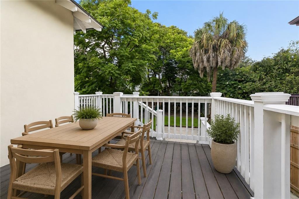 Wooden deck with an outdoor dining set, white railings, and leafy trees.