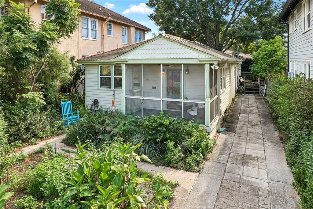 Light-colored home with a screened porch, paved side walkway, and leafy garden.