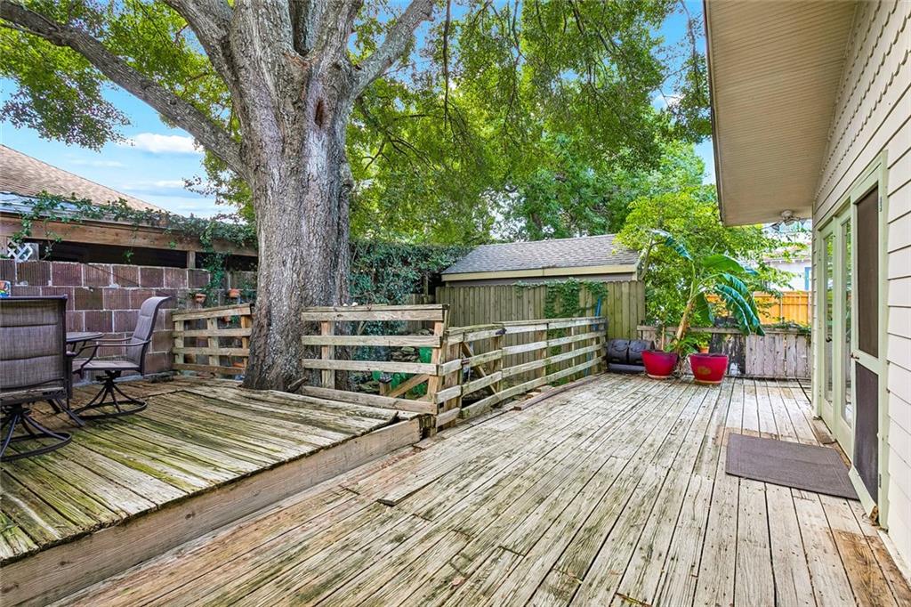 Wooden backyard deck beneath a large shade tree, with seating, planters, and a garden shed.