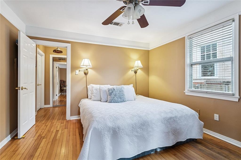 Bedroom with a white quilted bed, tan walls, hardwood floors, and a large window with blinds.