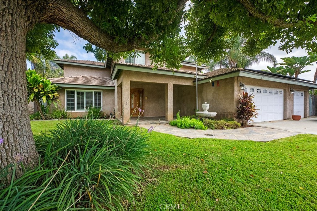 Two-story stucco home with a covered entry, white garage doors, and a mature shade tree.