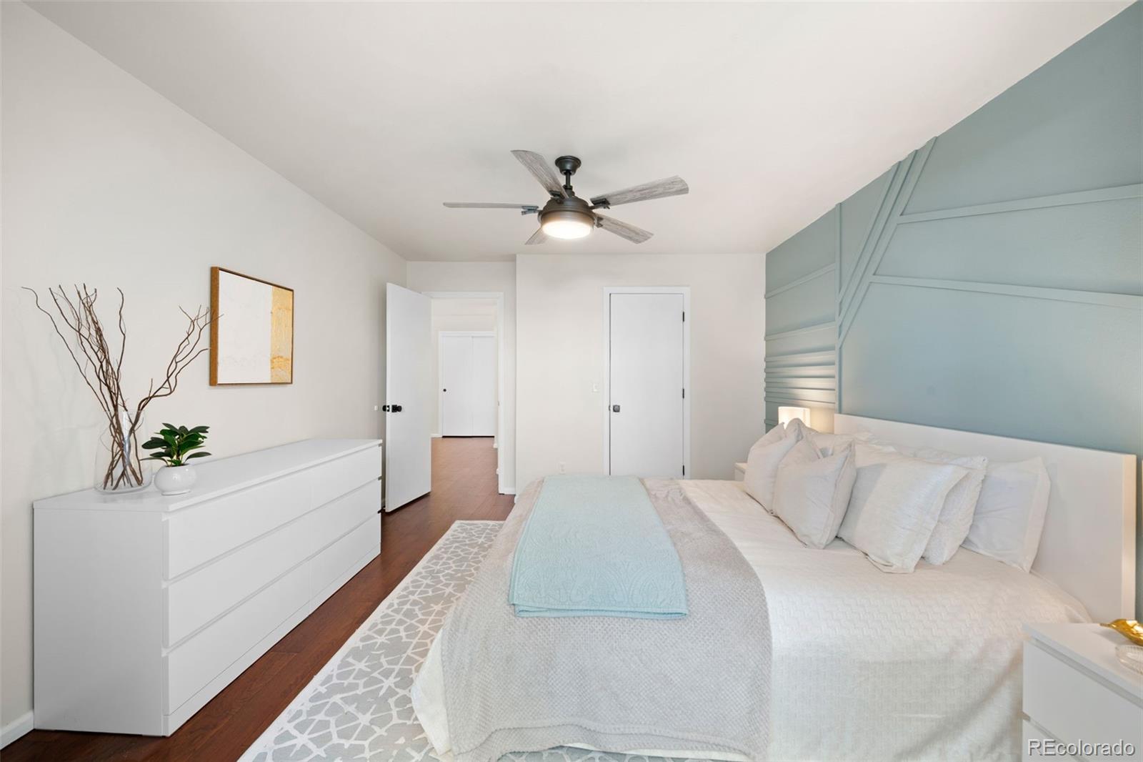 Staged bedroom with pale blue accent wall, white bed, and white dresser.