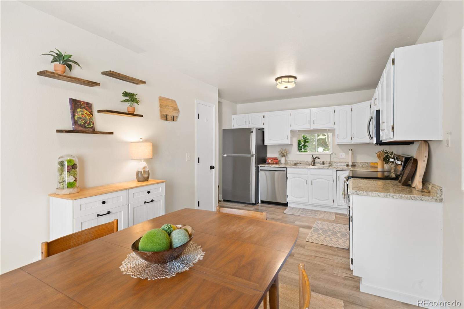 Bright kitchen with white cabinets, stainless steel appliances, and a wooden dining table.