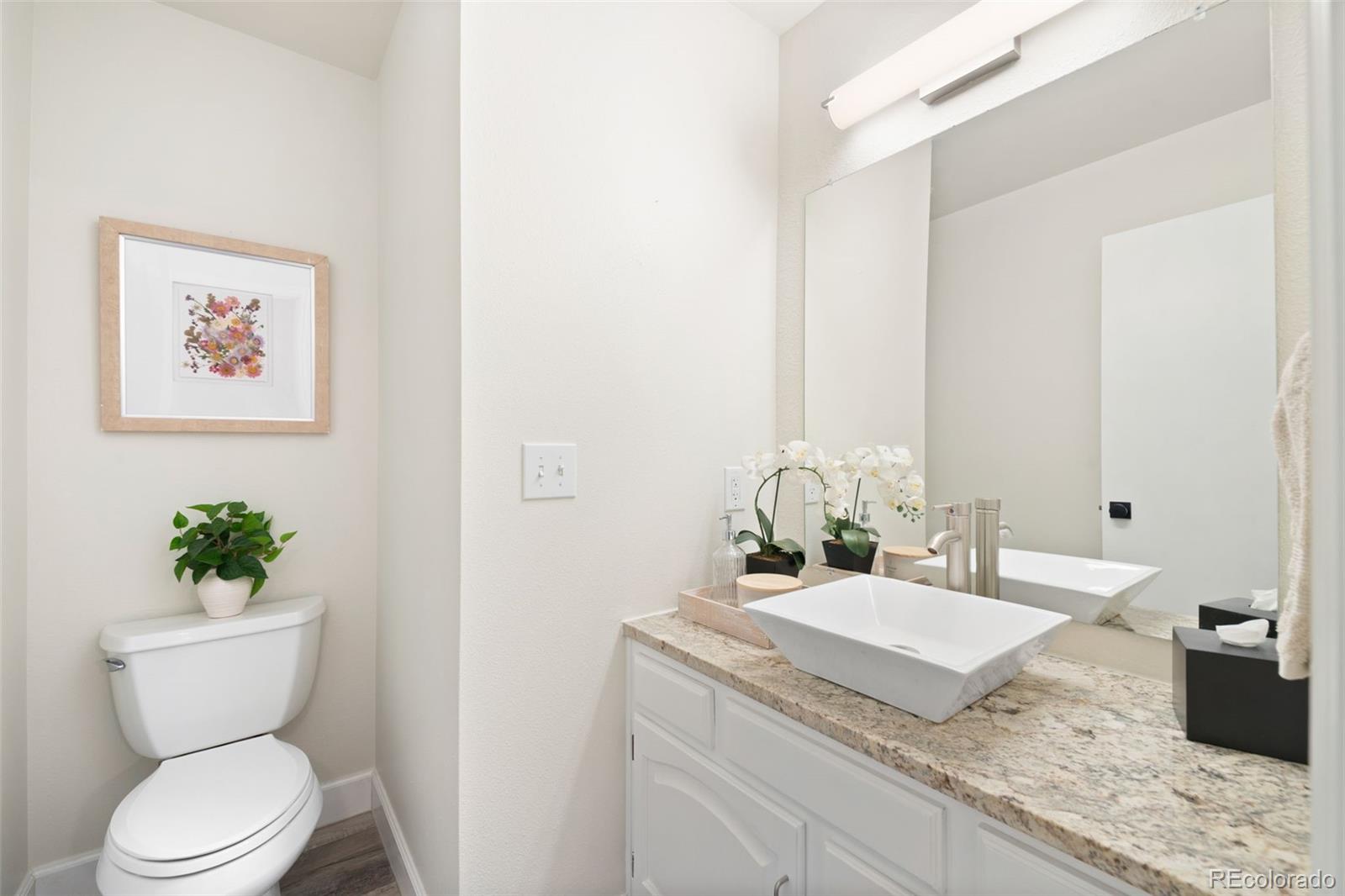 Bathroom with a vessel sink, granite countertop, large mirror, and toilet.