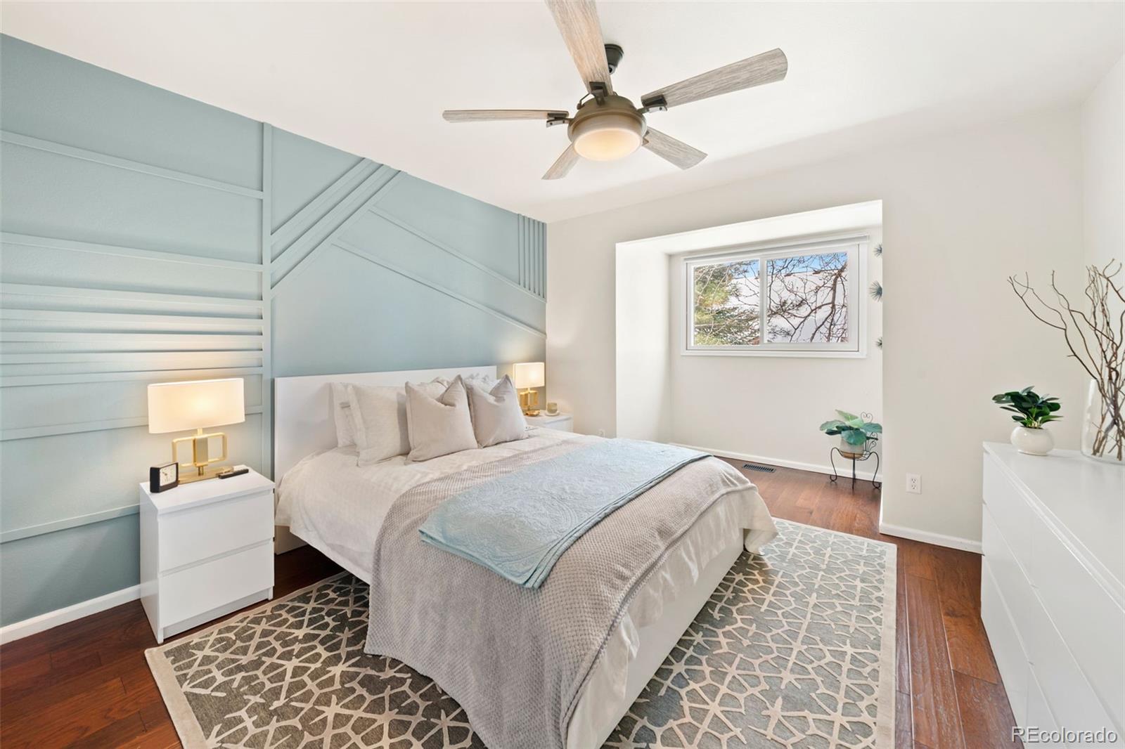Staged bedroom with a pale blue paneled accent wall, geometric rug, and ceiling fan.