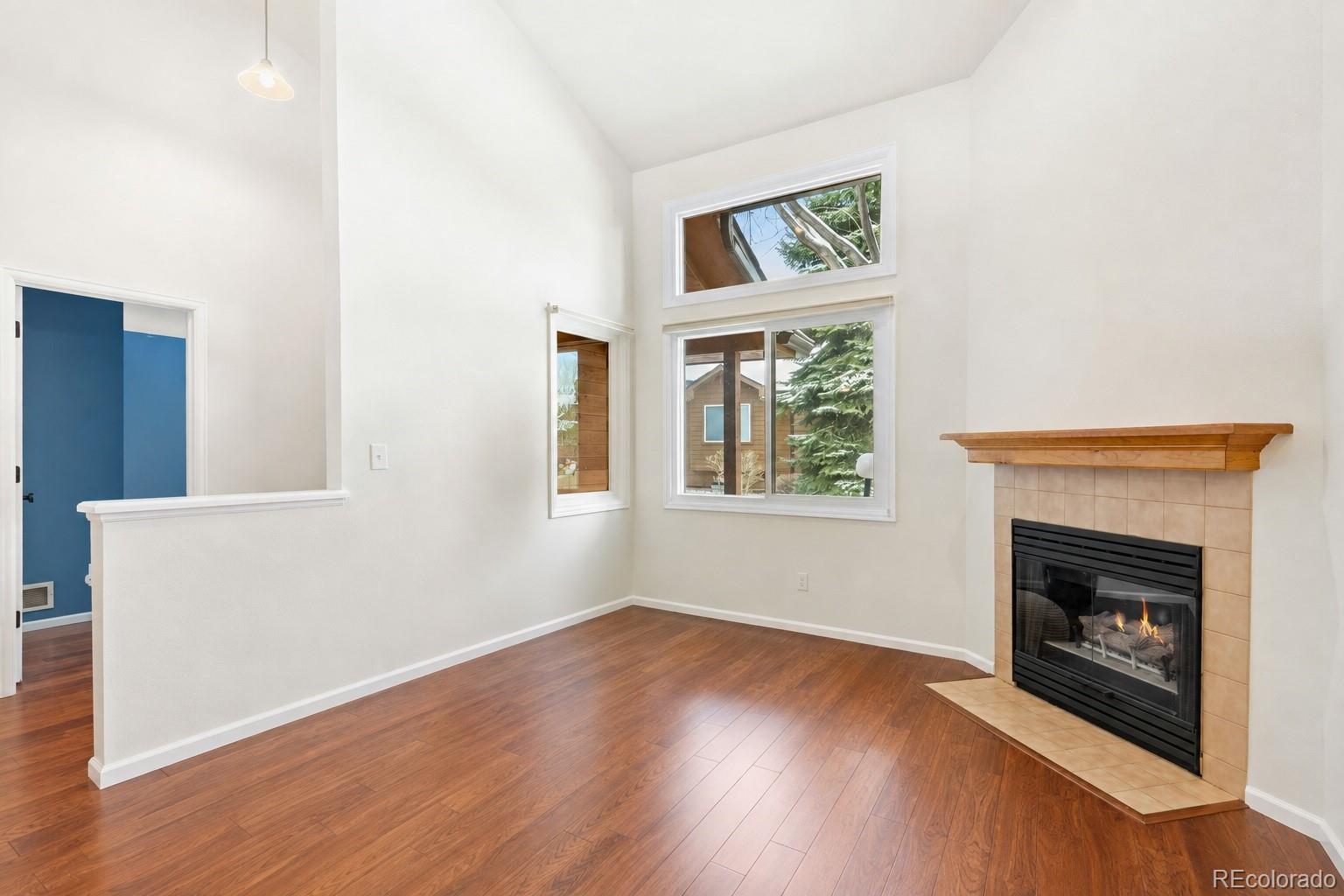 Empty living room with hardwood floors, tall windows, and a tiled fireplace with a wood mantel.