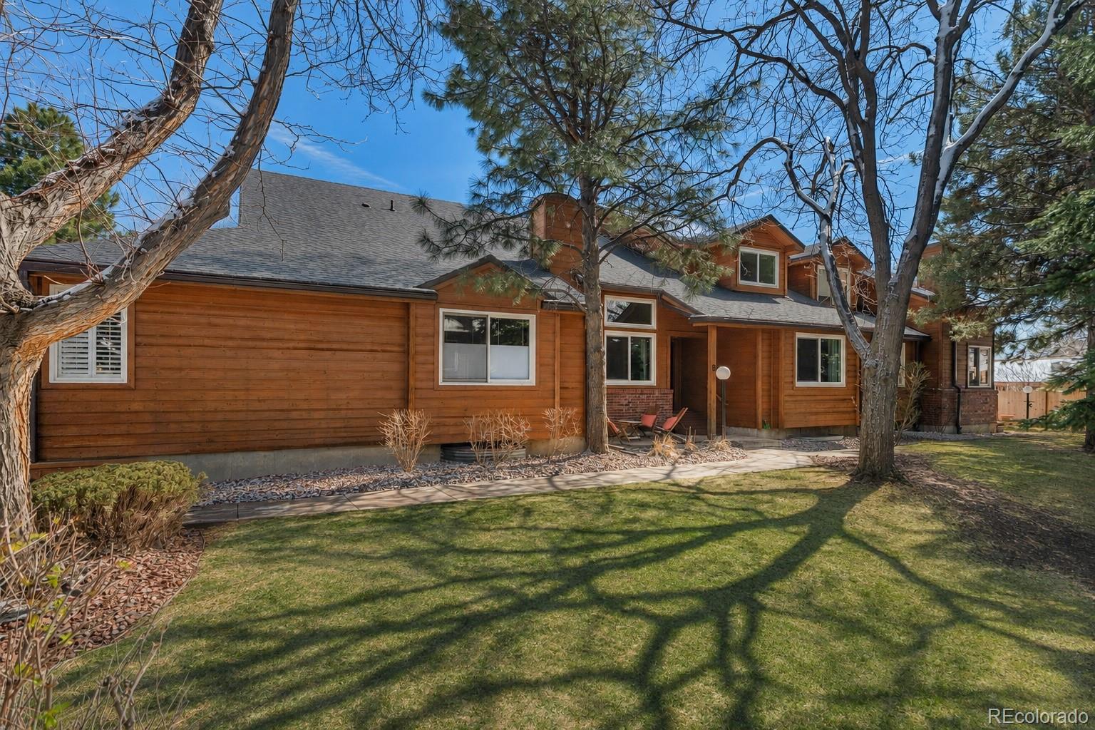 Wood-sided home with mature trees, a broad lawn, and a covered front entry.