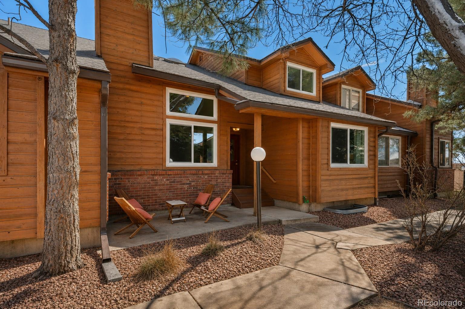 Wood-sided home with a covered patio, wooden chairs, and a curved walkway through rock landscaping.