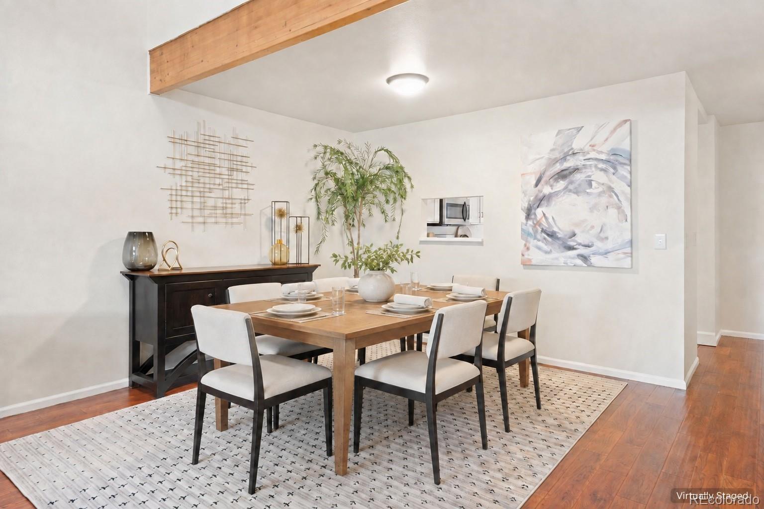 Staged dining room with a wood table, upholstered chairs, patterned rug, and kitchen pass-through.