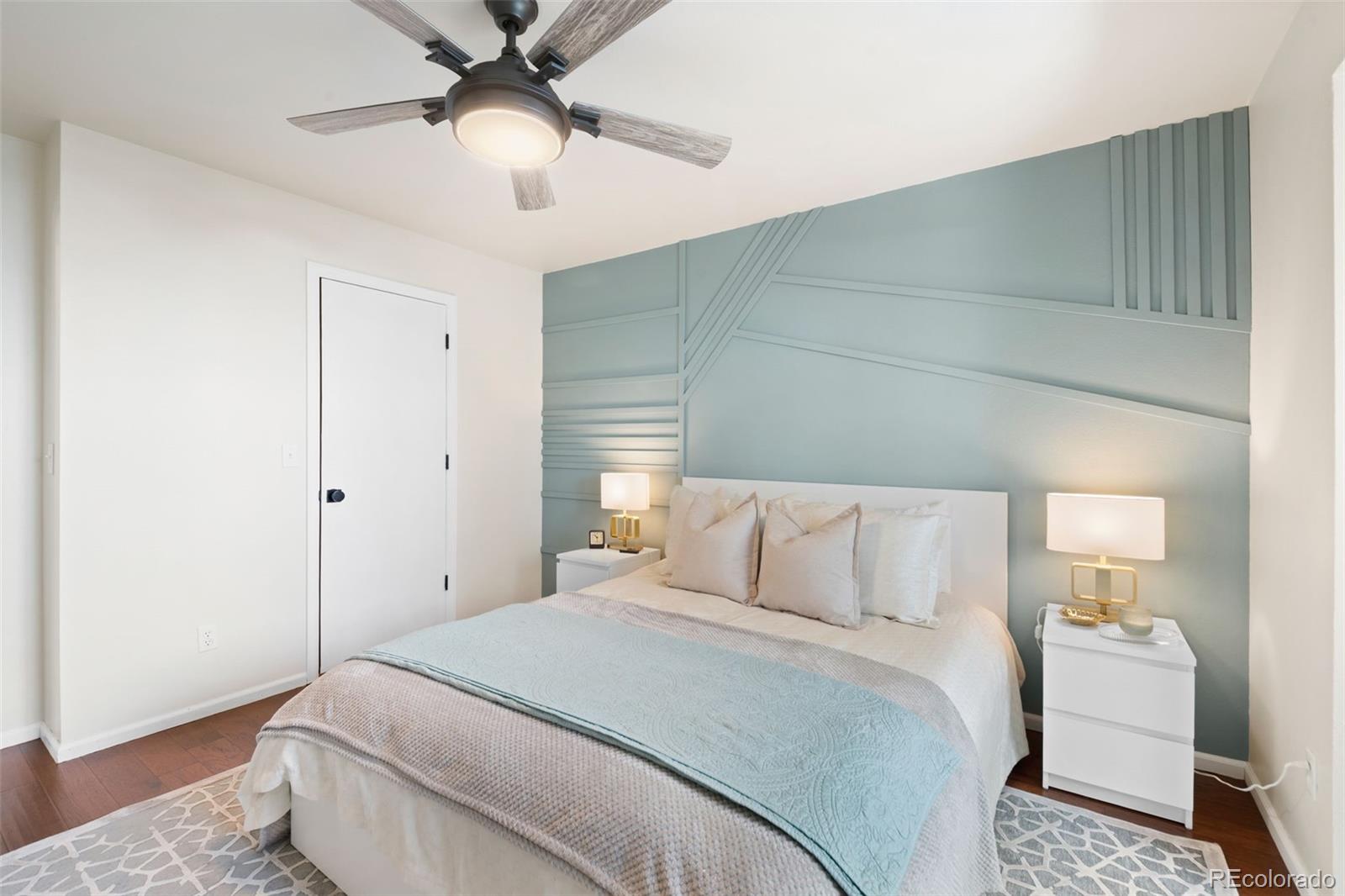 Staged bedroom with pale blue geometric accent wall, white bed, and ceiling fan.