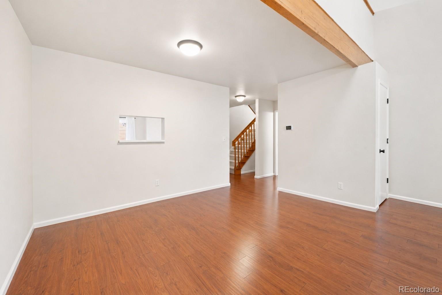 Empty room with hardwood floors, an exposed wood beam, and a staircase in the background.