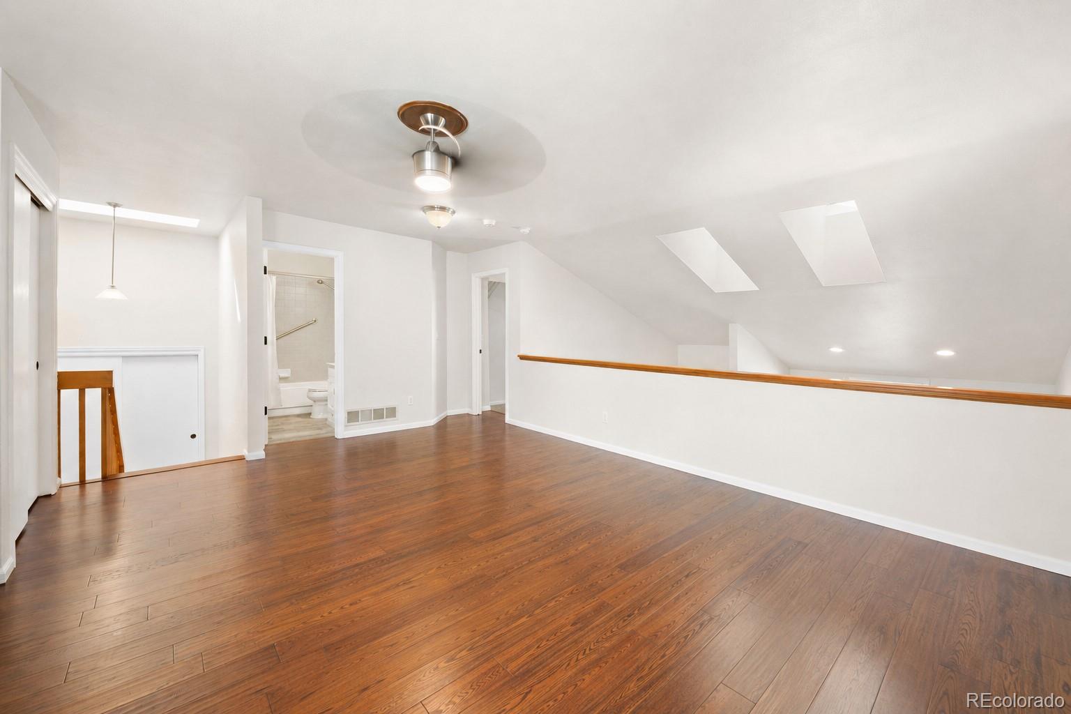 Unfurnished loft with wood floors, two skylights, and a railing overlooking the stairs.
