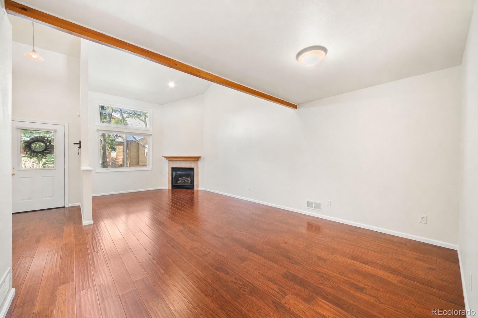 Empty living room with hardwood floors, a wood ceiling beam, and a fireplace