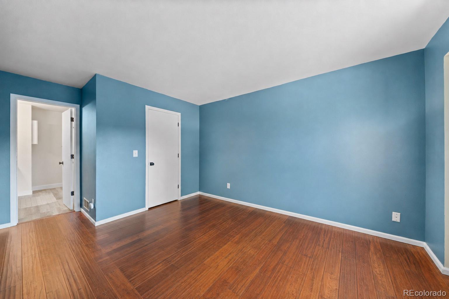 Vacant blue-walled room with wood flooring and an open doorway to a tiled area.