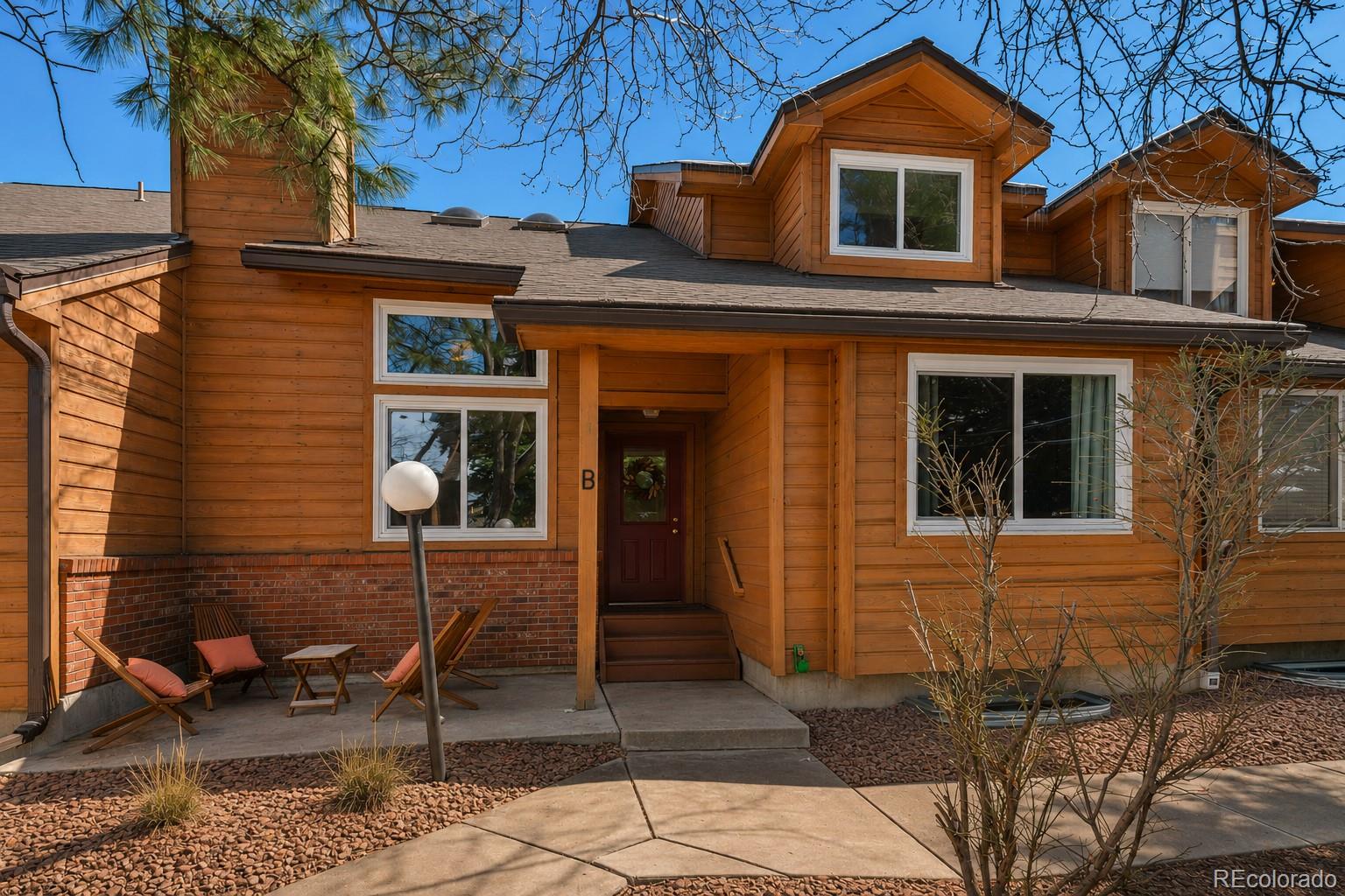Wood-sided two-story home with a covered entry marked B and a small patio with wooden chairs.