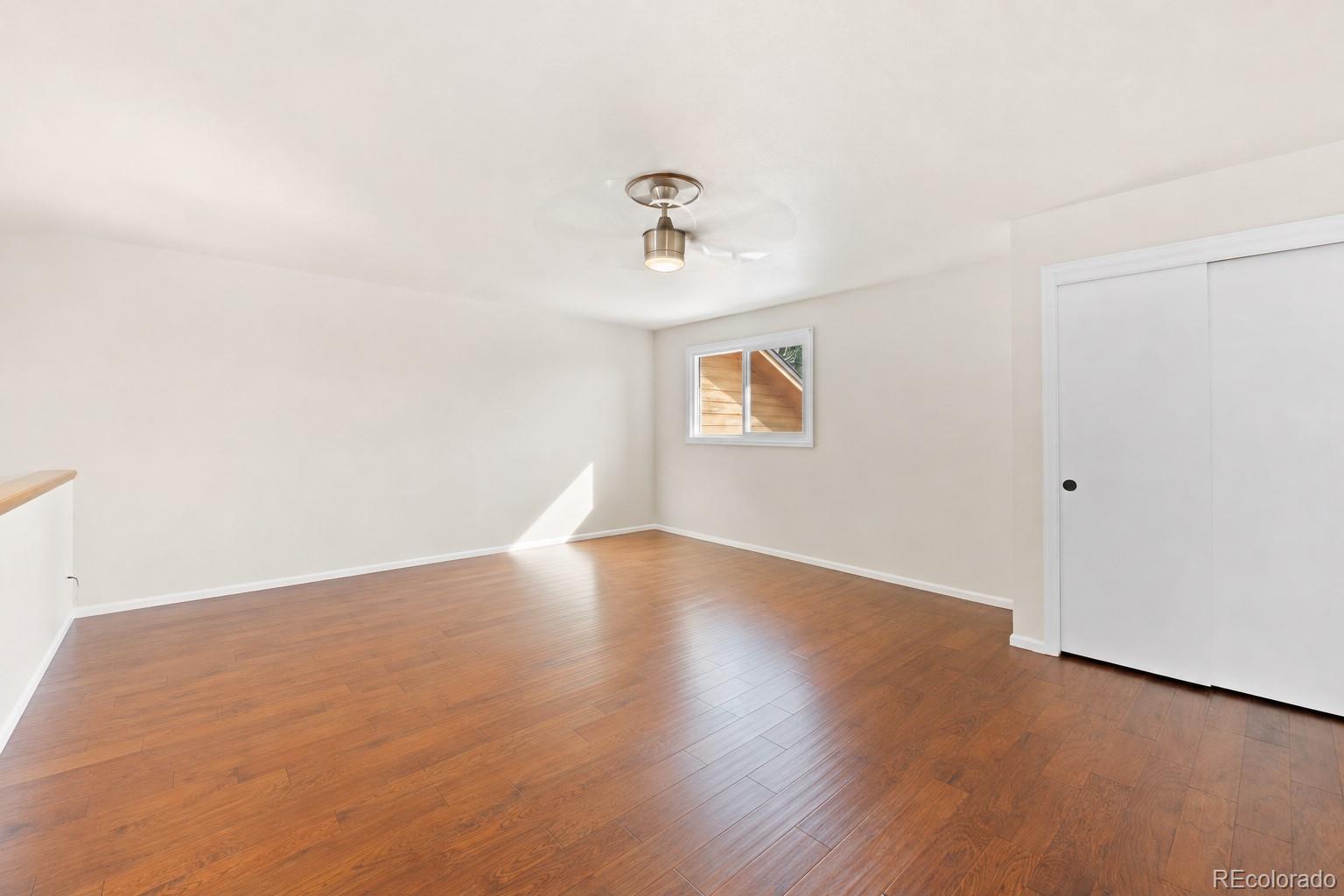 Empty room with hardwood floors, a sliding closet door, small window, and ceiling fan.