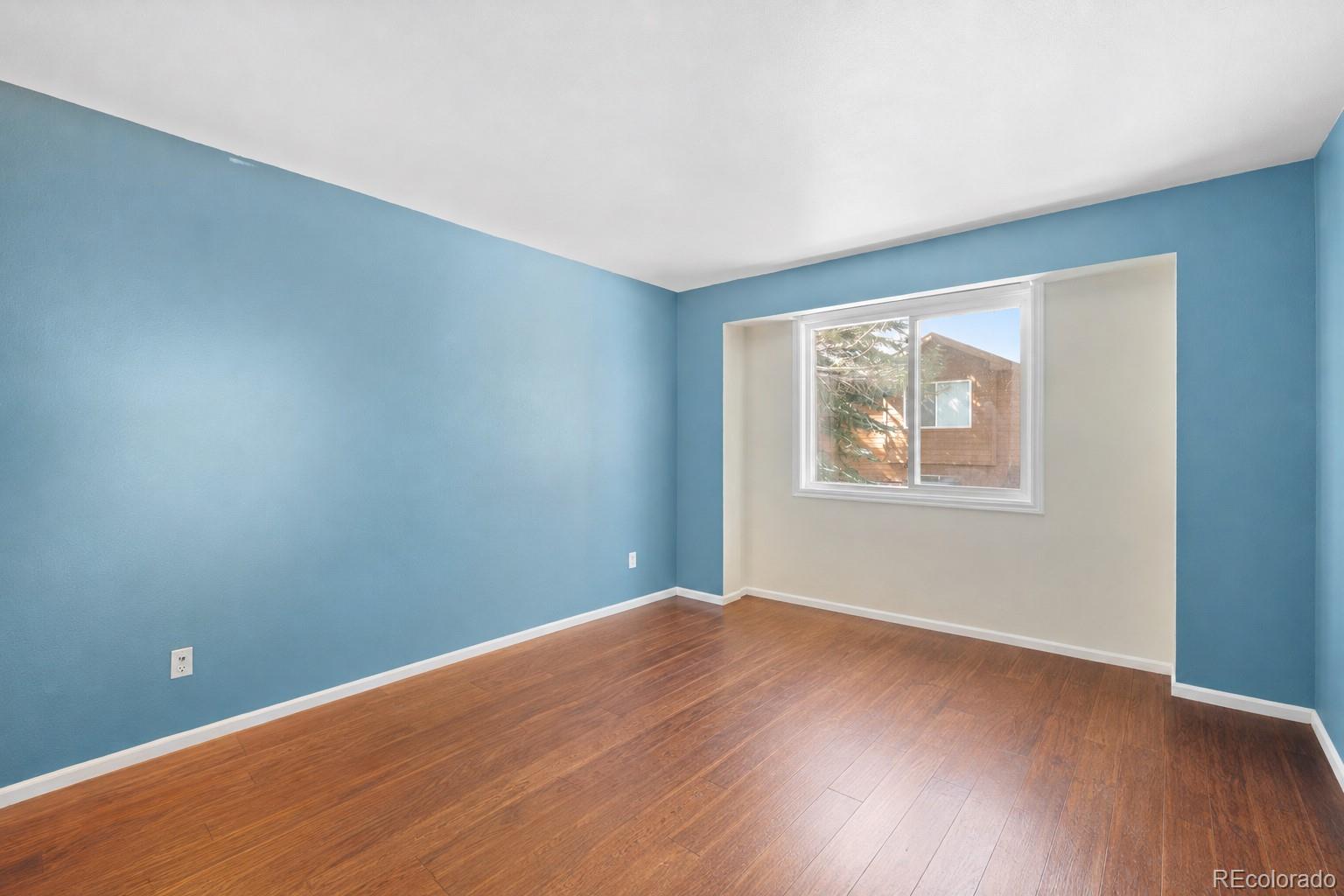 Empty room with blue walls, warm wood flooring, and a recessed window.