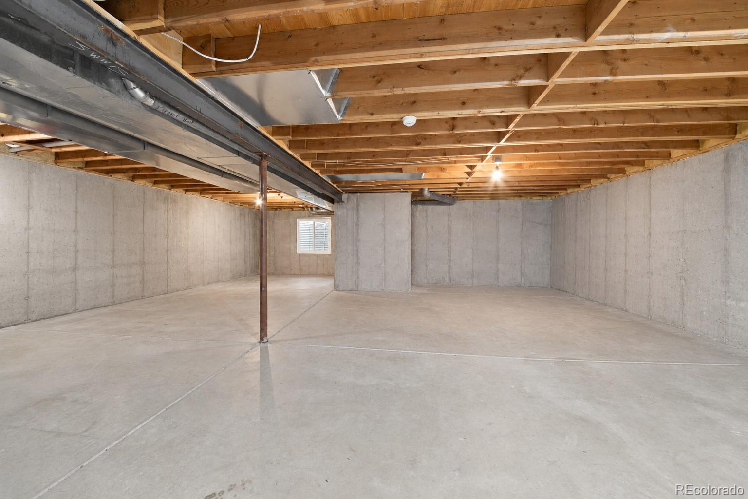 Unfinished basement with a broad concrete floor, exposed ceiling joists, and a small window.