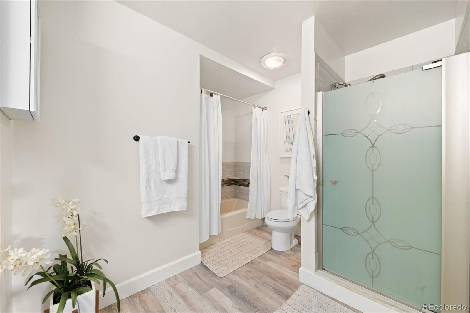 Bathroom with a frosted-glass shower, bathtub, and light wood-look flooring.