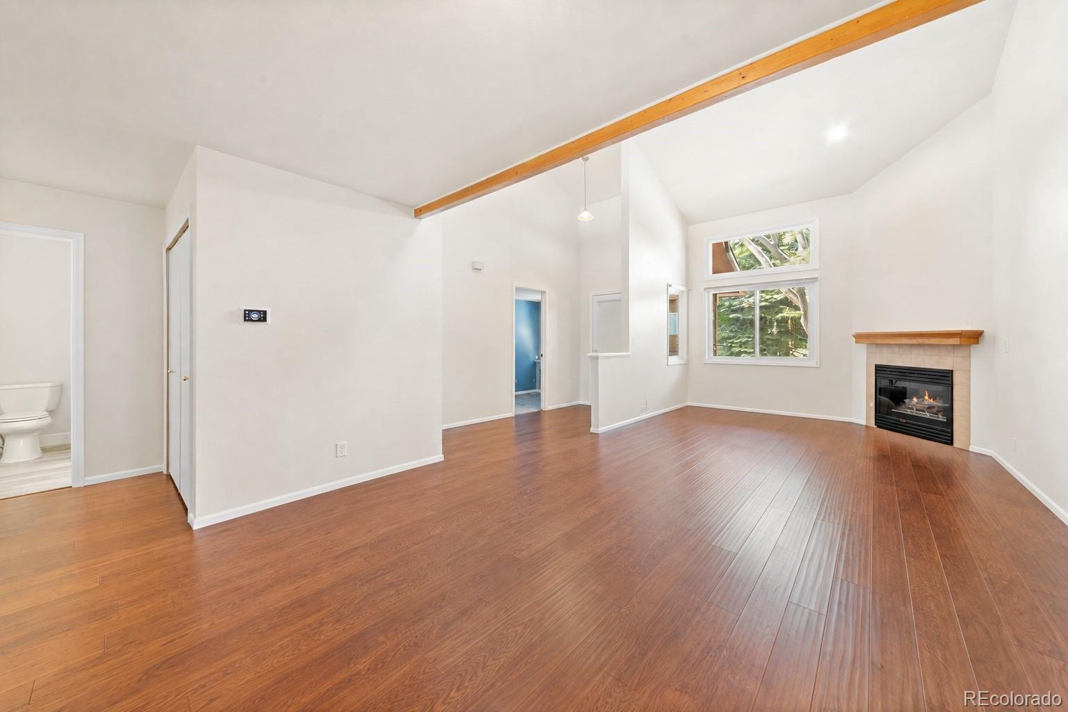 Vacant living room with vaulted ceiling, wood floors, large windows, and a gas fireplace.