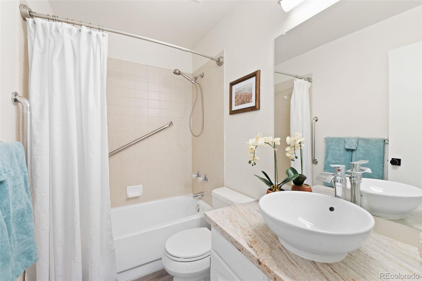 Bathroom with a tub-shower, grab bars, vessel sink, and orchid arrangement.