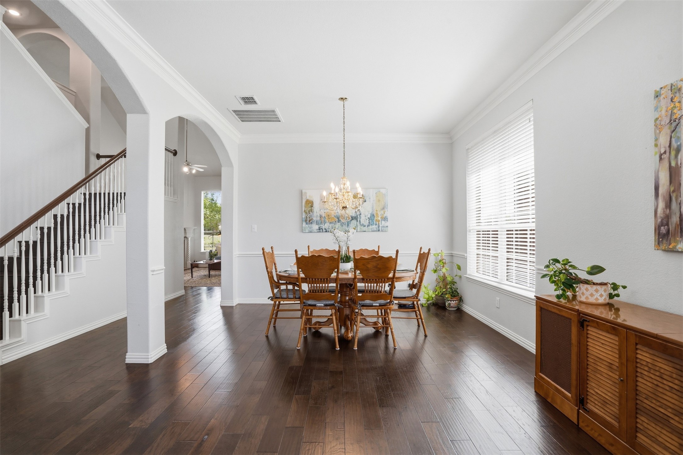 Dining room with a wooden table beneath a chandelier beside a staircase and arched doorway.