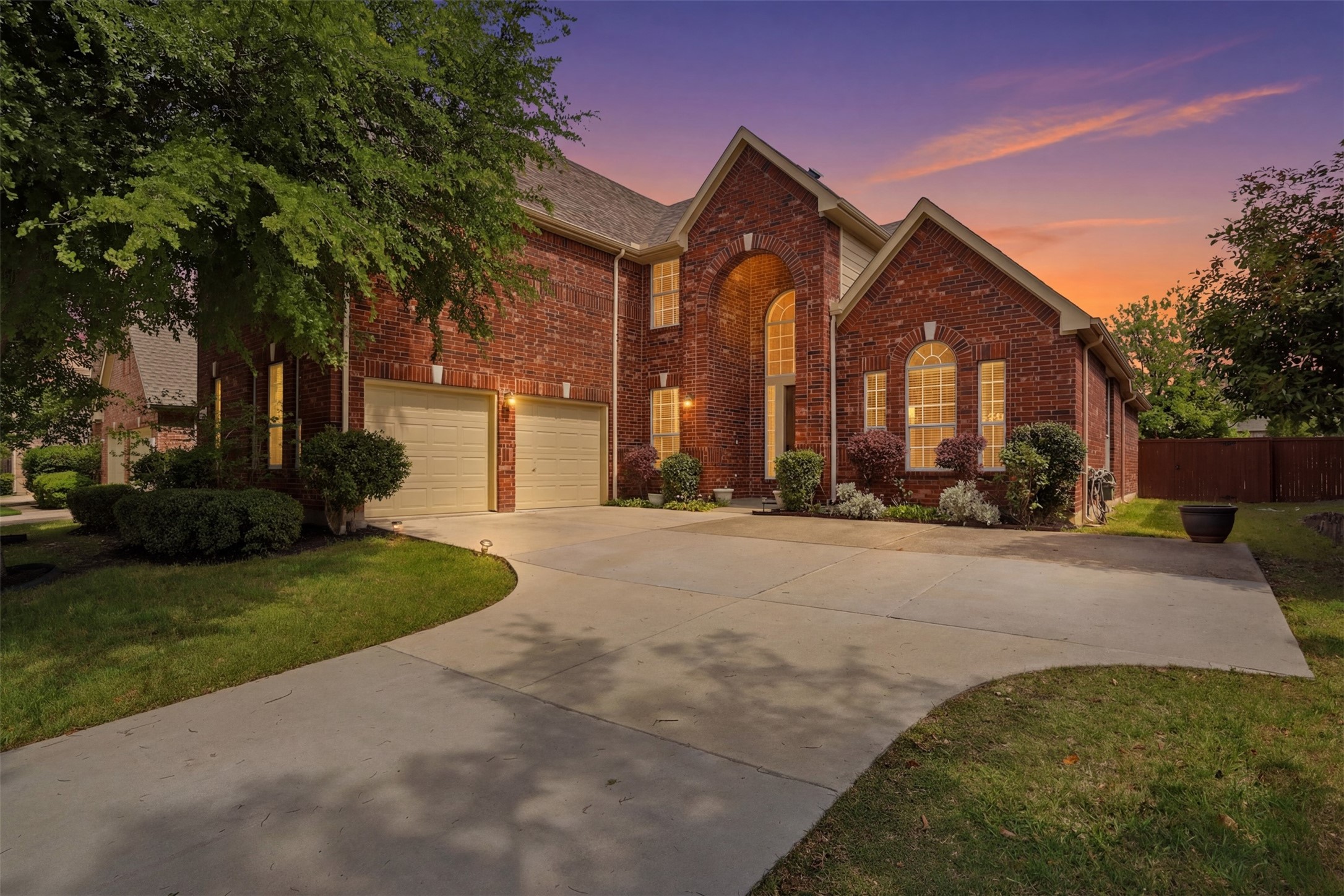 Two-story brick home with an arched entry and two-car garage at dusk.