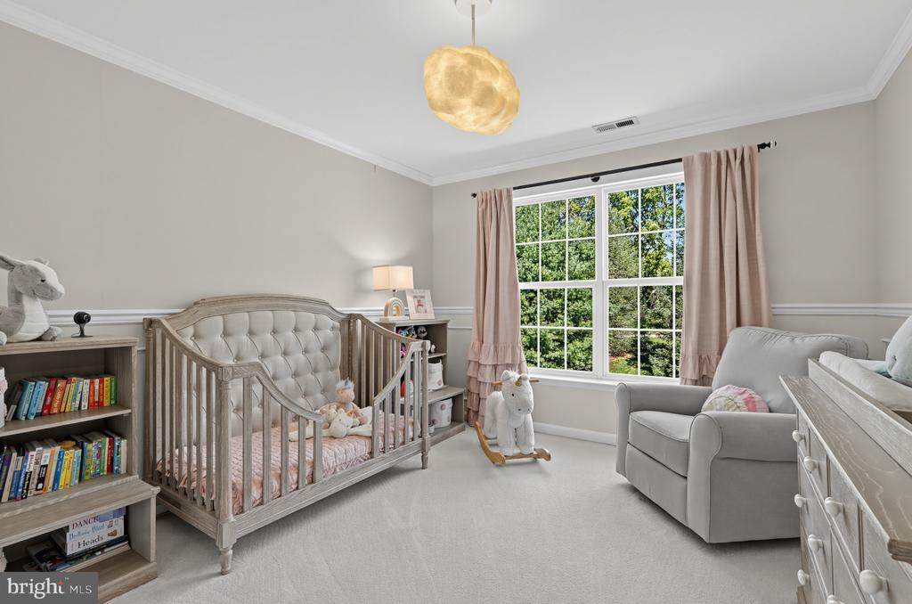 Nursery with a tufted gray crib, pink curtains, and a large window overlooking trees.