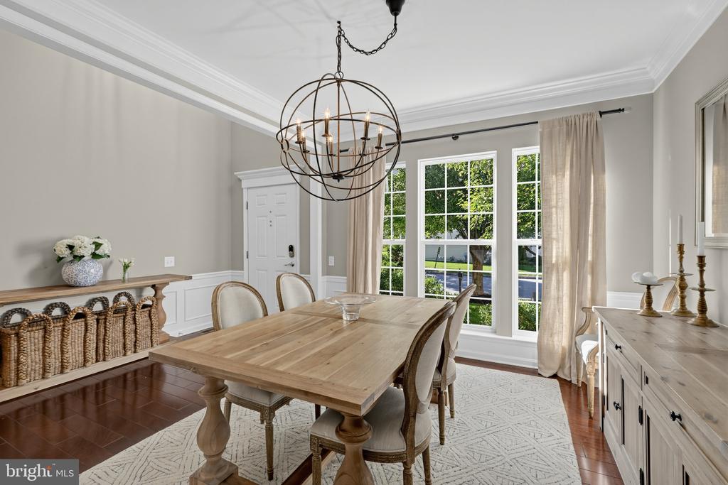 Dining room with a light wood table, globe chandelier, and tall curtained windows.