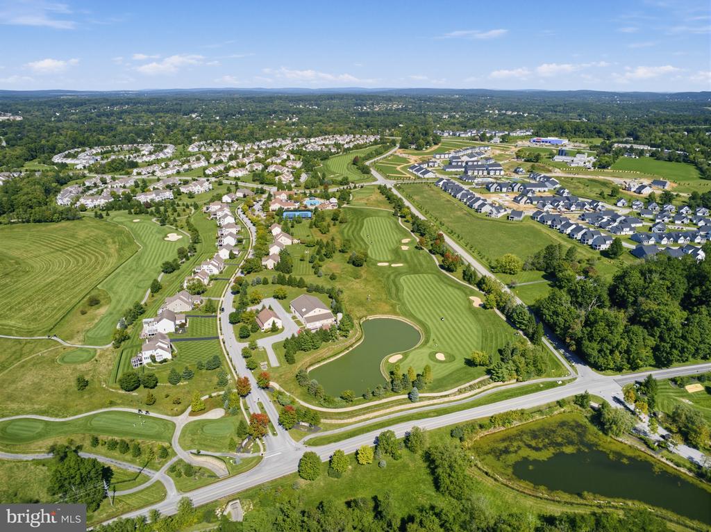 Aerial view of a golf course and surrounding homes, with striped fairways and a pond.