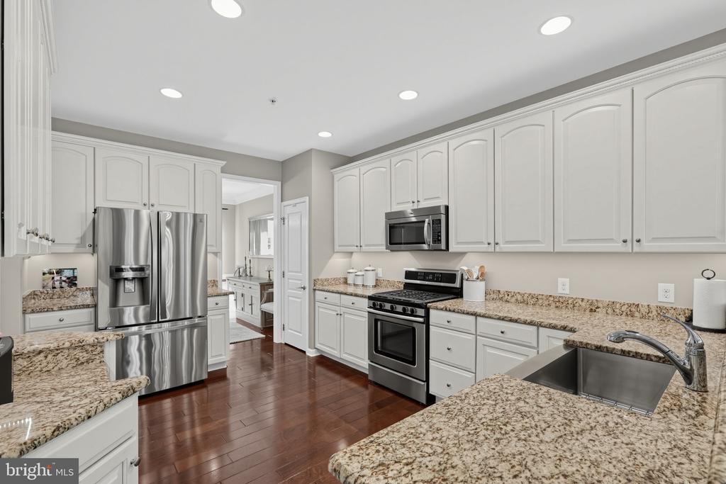 Kitchen with white cabinets, granite counters, stainless steel appliances, and dark hardwood floors.