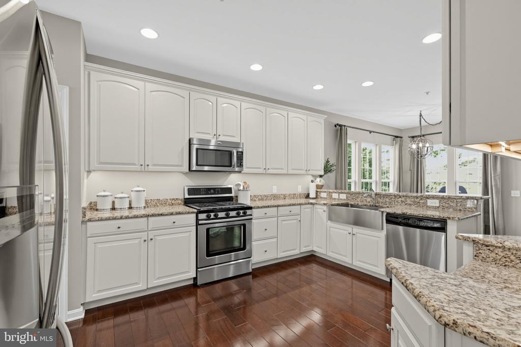 Kitchen with white cabinets, granite counters, stainless steel appliances, and dark wood flooring.