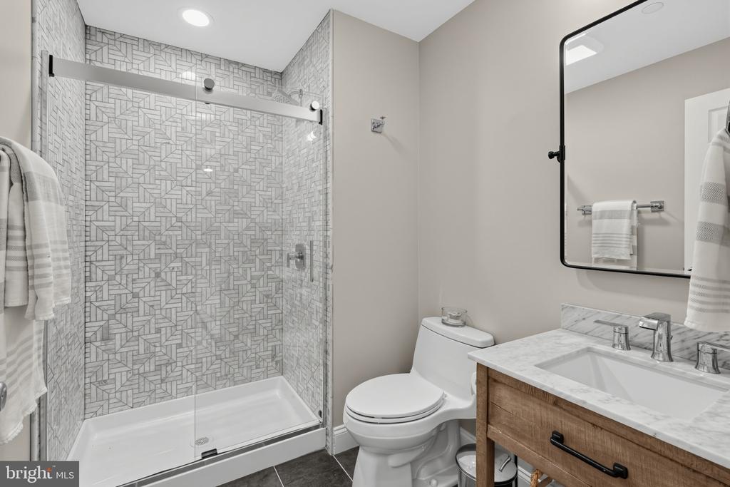 Bathroom with a patterned-tile glass shower and wood vanity topped with marble.