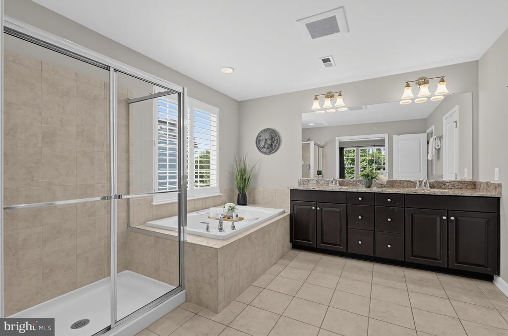 Bathroom with glass shower, built-in soaking tub, and long dark double vanity.