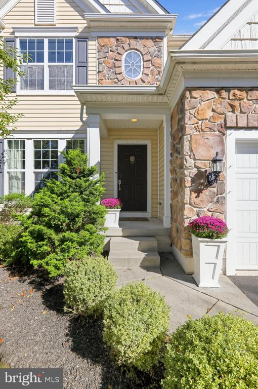 House entrance with stone facade, covered porch, and pink flowers in white planters.
